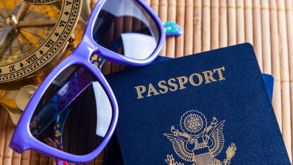 A passport, sunglasses, and compass of someone who is learning how to keep yourself safe while traveling
